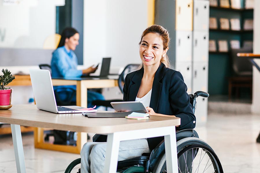 Employee Benefits - Businesswoman Using a Wheelchair in an Office, Smiling, at Her Desk