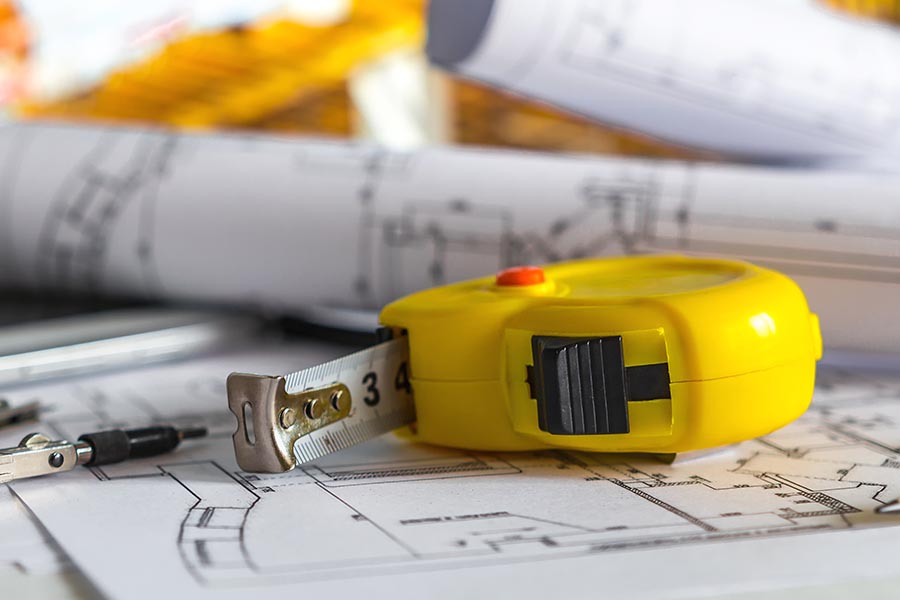 Specialized Business Insurance - Construction Tools and Plans Scattered on a Table, Bright Yellow Measuring Tape up Front